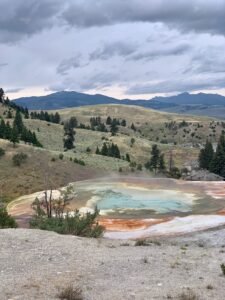 Colorful yellowstone geyser with a view of rolling hills and mountains in the distance
